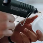 person placing glue on plastic with a hot glue gun